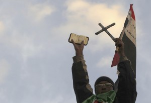 Cette photo, prise pendant une manifestation monstre sur la Place Tahir, en janvier 2011, montre un manifestant brandissant la croix des chrétiens, le coran, des musulmans et le drapeau national (photo CNS/Amr Abdallah Dalsh, Reuters)