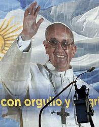 Un homme entretien un feu de circulation devant un immense poster du pape à Buenos Aires. Le texte se lit comme suit: La ville célèbre le pape François avec fierté et joie (photo CNS/Marcos Brindicci, Reuters).