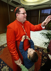 Le cardianal Gérald Cyprien Lacroix salue des fidèles pendant qu'un garçon tire sur sa croix pastorale lors de la réception en l'honneur des nouveaux cardinaux dans la Salle d'audience Paul VI du Vatican (photo CNS/Paul Haring).