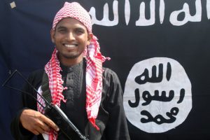  Cette photo publiée par l’État islamique représente un homme identifié (par l'État islamique) comme étant Abu Umeer al-Benghali, l'un des tireurs qui a conduit l'attaque dans la capitale Dhaka le 1er juillet 2016, durant laquelle 20 otages ont été abattus dans un restaurant. Il pose avec un fusil devant le drapeau du groupe jihadiste de l'État islamique (lieu non-révélé). © AFP 